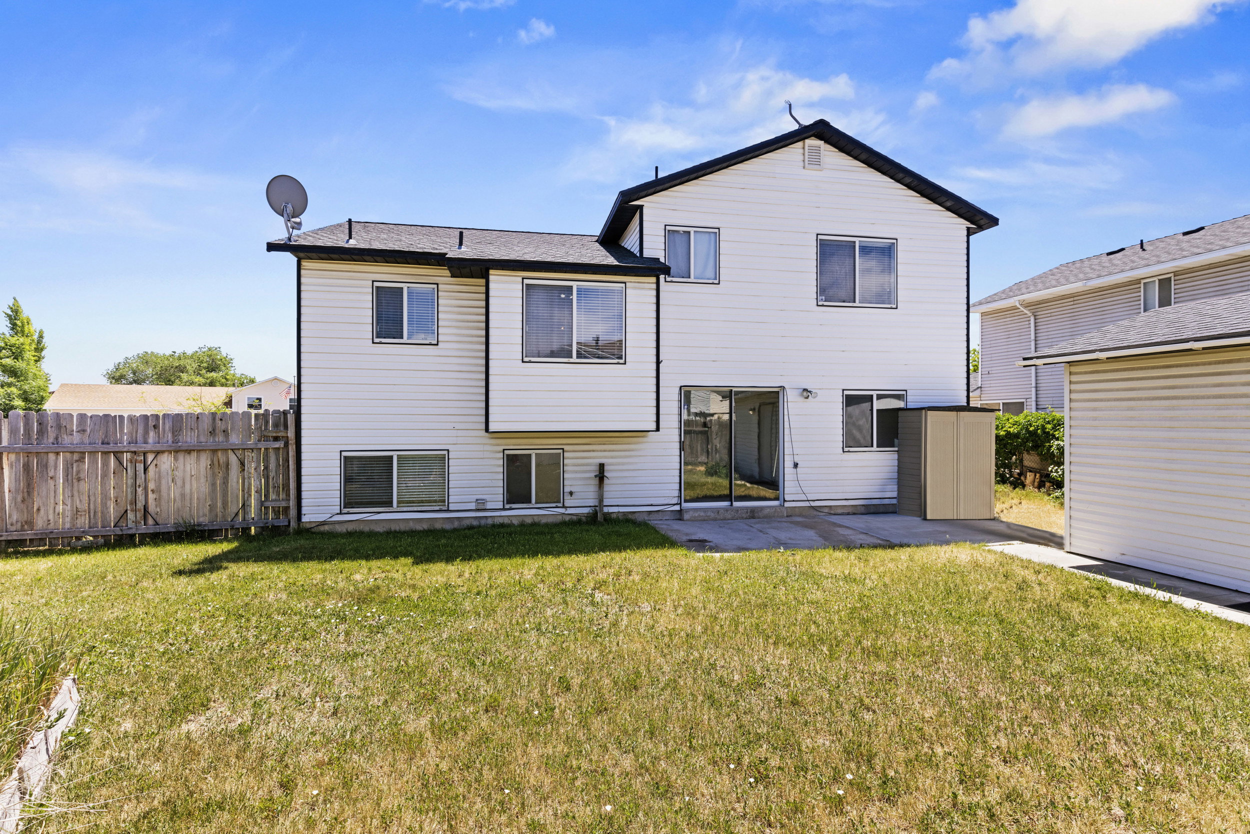 Rear exterior featuring white siding, a black shingled roof, sliding glass patio doors, and a concrete patio pad