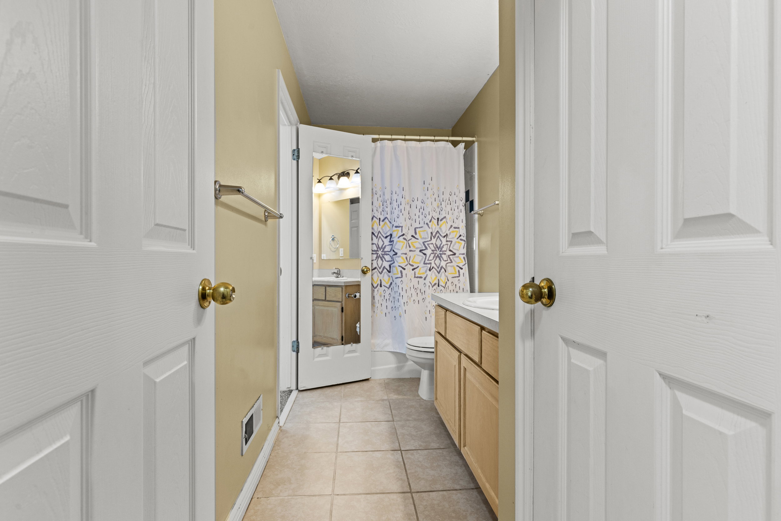 Bathroom featuring tile flooring, a light wood-finish vanity with a white countertop, and a shower with a patterned curtain