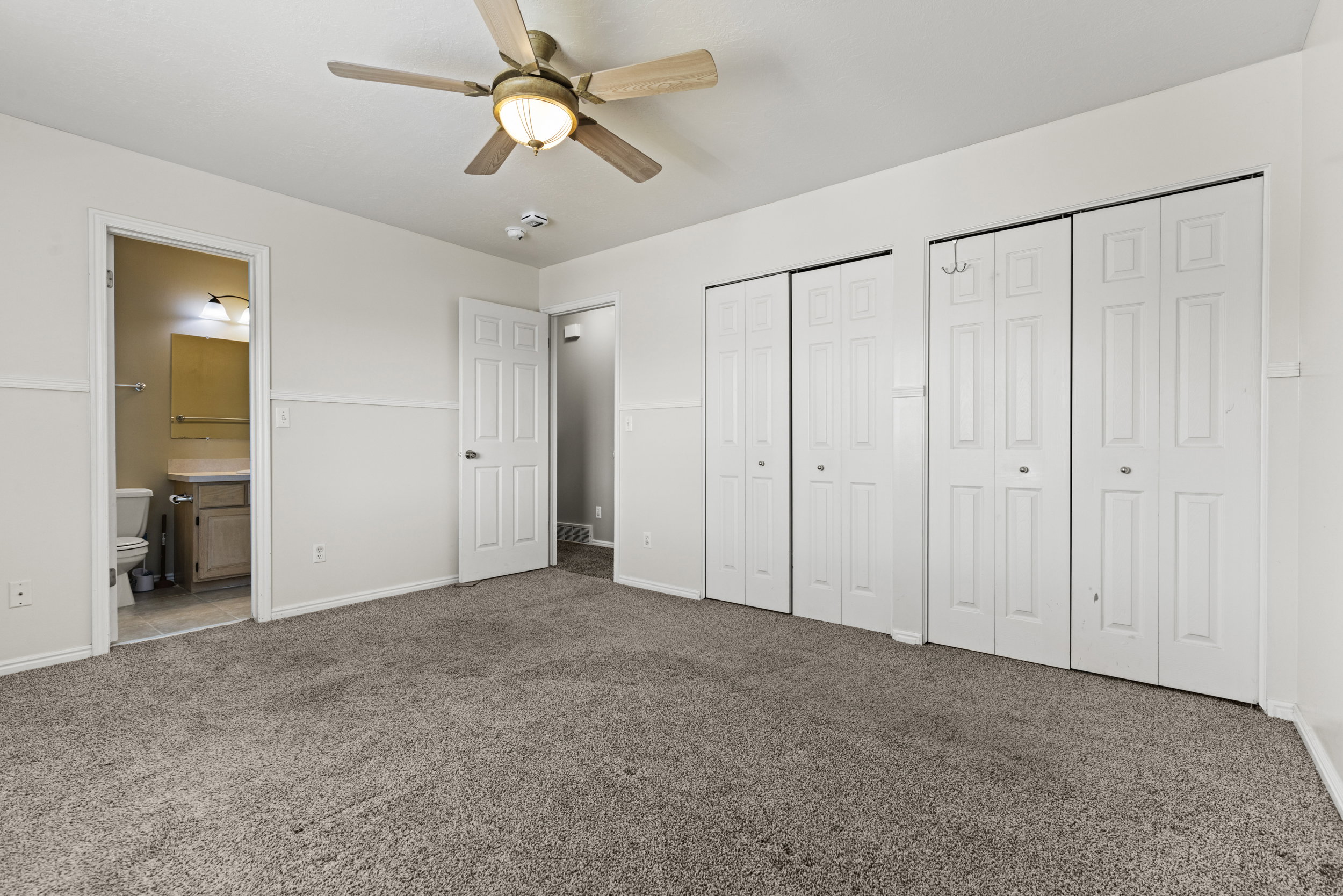 Spacious room featuring neutral carpet, white paneled doors, and a ceiling fan with integrated lighting