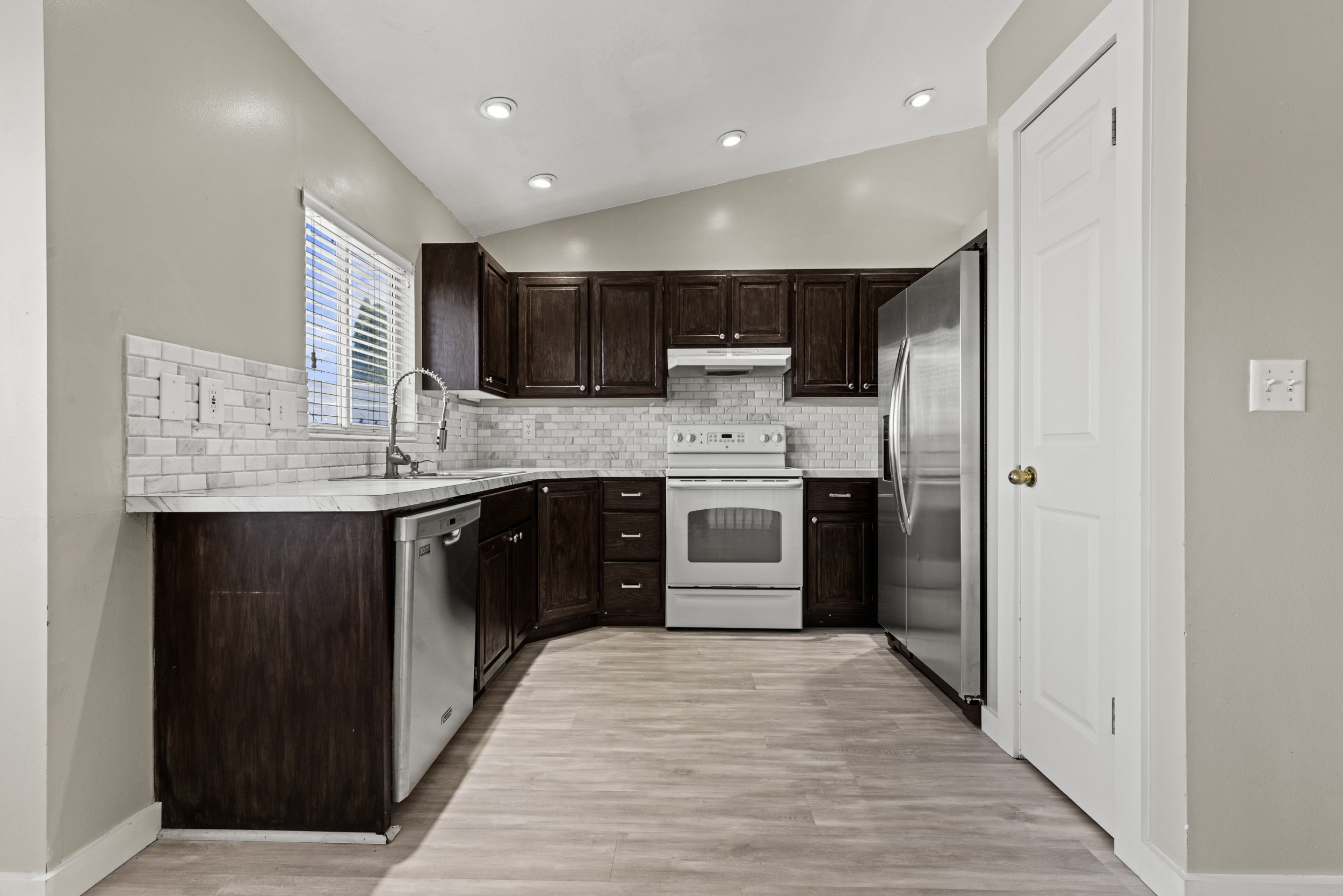 Kitchen featuring dark wood cabinetry, light-toned wood-finish flooring, white subway tile backsplash, stainless steel appliances, and recessed lighting