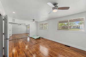 Spacious interior room featuring rich wood-finish flooring, two modern ceiling fans with integrated lighting, and multiple windows providing natural illumination