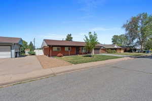 Red brick ranch-style exterior with a brown shingle roof, established front yard landscaping, and an attached garage
