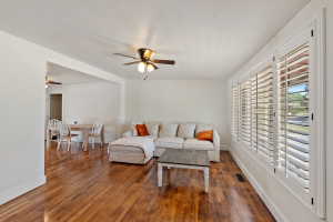 Spacious living area featuring wood-finish flooring, white walls, and a ceiling fan with integrated lighting