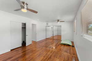 Spacious room featuring wood-finish flooring, two ceiling fans with integrated lighting, a mirrored closet, and a window with blinds