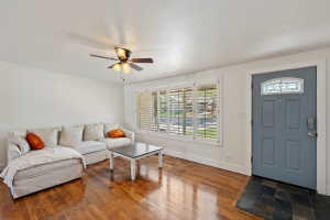 Living area featuring rich wood-finish flooring, white walls, and a ceiling fan with integrated lighting