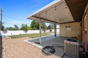 Expansive concrete patio with a full overhead covering, string lighting, and direct access to a gravel and lawn area