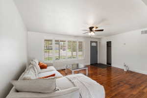 Spacious living area featuring wood-finish flooring, white walls, and a multi-panel window with louvered shutters