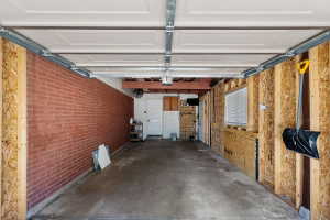 Spacious garage featuring a concrete floor, exposed brick wall, white paneled garage door, and a built-in window with white blinds
