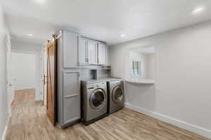 Dedicated laundry area featuring modern front-loading appliances, light gray cabinetry, and wood-finish flooring