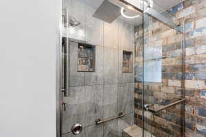 Glass-enclosed shower featuring a rainfall showerhead, dual tiled wall niches, a built-in bench, and a unique multi-toned brick-patterned tile wall