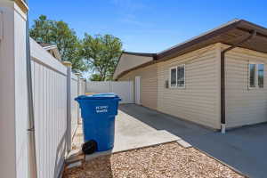 Side access concrete driveway featuring a white privacy fence and gravel landscaping