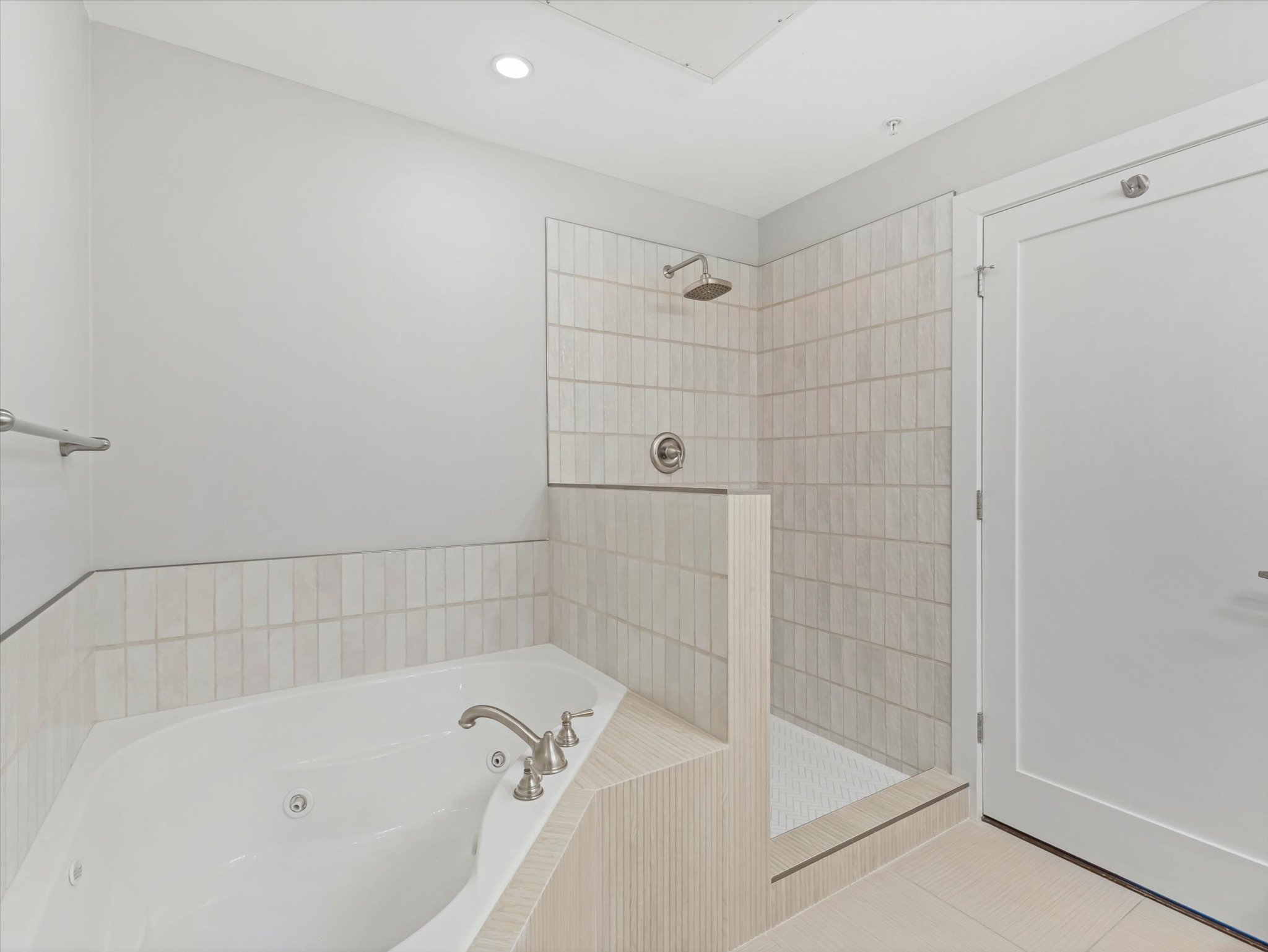 Bathroom featuring a jetted tub, a walk-in shower with a rain showerhead, light-colored vertical tile, and coordinating floor tile