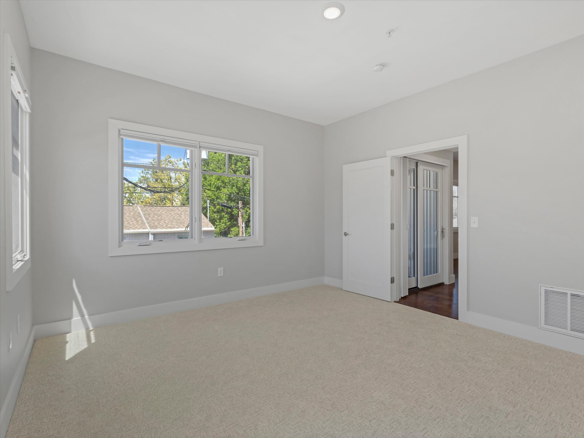 Carpeted interior space featuring white trim, multiple windows, recessed lighting, and a doorway with French doors