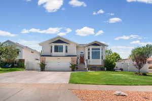 Suburban residence featuring a two-car garage, bay windows, brick accents, a manicured lawn, and a paved driveway