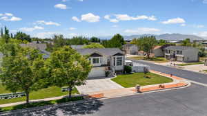 Contemporary residence featuring a two-car garage, concrete driveway, front lawn with mature trees, white picket fence, and a corner lot location