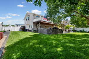 Expansive green lawn featuring a stone-clad outdoor kitchen, a covered patio area, and a second-story balcony