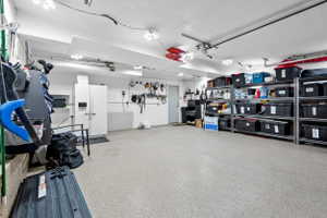Spacious garage featuring epoxy flooring, extensive built-in shelving, ample overhead lighting, and a side access door