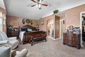 Spacious bedroom featuring vaulted ceilings, carpet flooring, a ceiling fan, and access to an adjoining bathroom