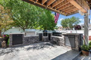 Outdoor kitchen featuring stone veneer base, light-toned countertops, built-in stainless steel grill, and additional cooking elements