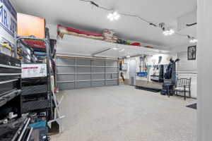 Spacious garage featuring a large overhead door, speckled epoxy flooring, overhead track lighting, and a substantial overhead storage shelf