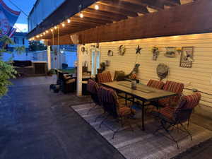 Covered patio featuring exposed wood beams, string lighting, and a built-in outdoor kitchen with stone veneer detailing