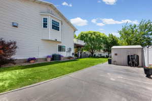 Expansive paved driveway alongside a manicured lawn, featuring a bay window, a storage shed, and a privacy fence