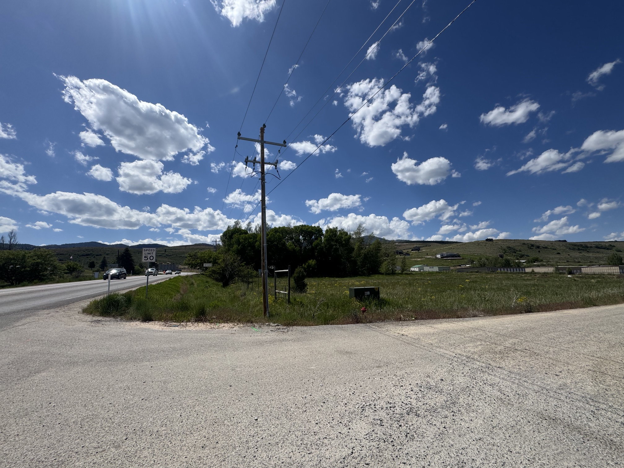 Expansive undeveloped land with a partial paved road frontage and distant hillside backdrop