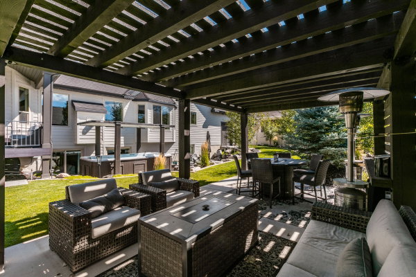 Spacious outdoor patio featuring a dark-stained pergola, concrete flooring, stone accents, and a built-in hot tub
