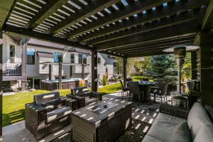 Spacious outdoor patio featuring a dark-stained pergola, concrete flooring, stone accents, and a built-in hot tub