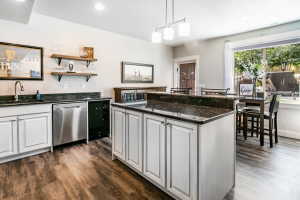Kitchenette featuring white cabinetry, dark stone countertops, wood-finish flooring, a stainless steel dishwasher, and a built-in sink