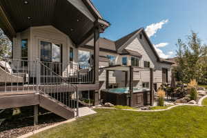 Expansive backyard featuring a manicured lawn, a multi-level deck with metal railings, a built-in hot tub with an overhead pergola, and a stone-lined garden bed with mature landscaping