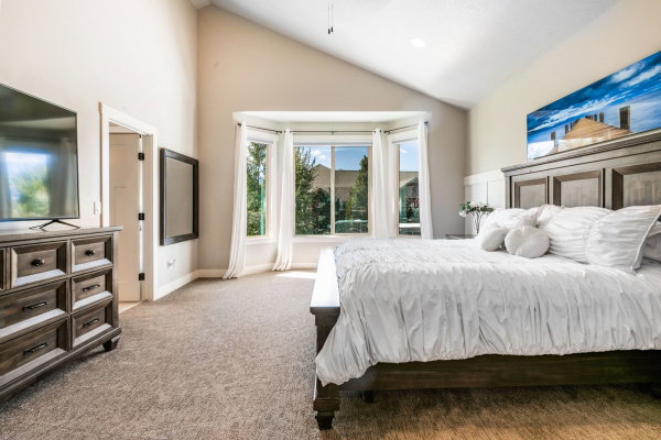 Carpeted bedroom featuring a vaulted ceiling, a bay window with natural light, and a paneled accent wall