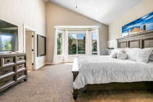 Carpeted bedroom featuring a vaulted ceiling, a bay window with natural light, and a paneled accent wall