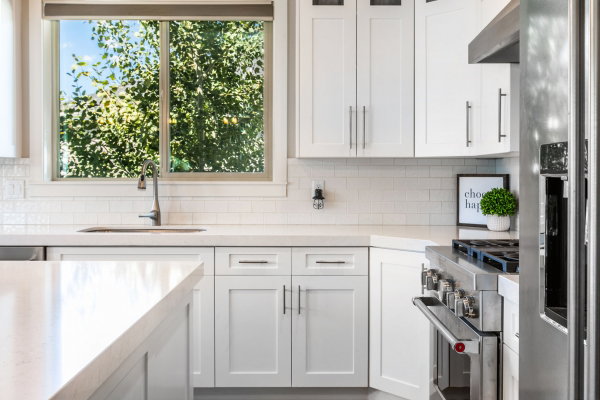 Modern kitchen featuring white shaker cabinetry, light countertops, subway tile backsplash, stainless steel appliances, and a kitchen island
