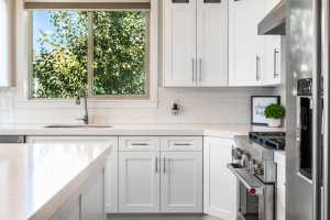Modern kitchen featuring white shaker cabinetry, light countertops, subway tile backsplash, stainless steel appliances, and a kitchen island