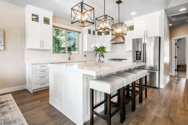 Bright kitchen featuring a central island with countertop seating, white shaker cabinetry, stainless steel appliances, and wood-finish flooring