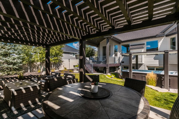 Spacious outdoor patio featuring a slatted pergola, paver flooring, and a round stone-finish table