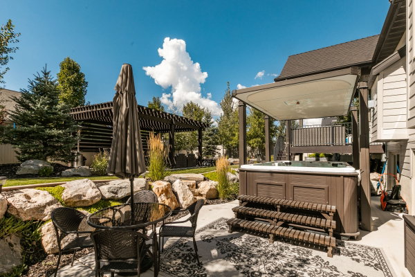 Outdoor living space featuring a covered hot tub, a separate slatted pergola, and a rock garden with mature trees