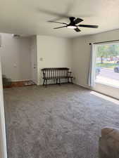 Spacious room featuring neutral carpeting, a modern ceiling fan with integrated lighting, a large window with white trim, and a white entry door