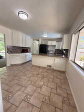 Kitchen featuring light-toned tile flooring with decorative inserts, white cabinetry, dark speckled countertops, and a central island with a breakfast bar