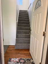 Entryway featuring wood flooring, a white paneled door with a decorative glass insert, and carpeted stairs with a white handrail