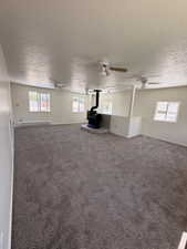 Spacious interior featuring a central black wood-burning stove on a stone hearth, neutral wall paint, and multiple ceiling fans