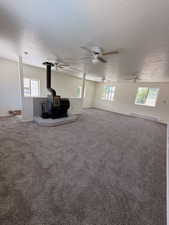 Spacious room featuring a central wood-burning stove with a stone hearth, multiple ceiling fans, textured ceilings, and wall-to-wall carpeting