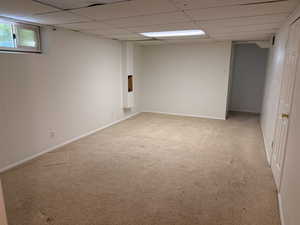 Spacious room featuring neutral carpet flooring, white painted walls, and a drop ceiling with integrated lighting