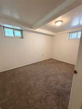 Carpeted room featuring white walls, exposed ceiling beams, and two windows