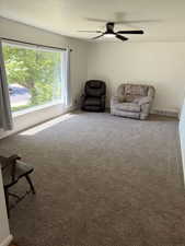 Spacious room featuring a large picture window, textured carpet flooring, a contemporary ceiling fan with integrated lighting, and neutral wall tones