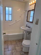 Bathroom featuring a pedestal sink, white tile shower surround, and a tub with integrated grab bar
