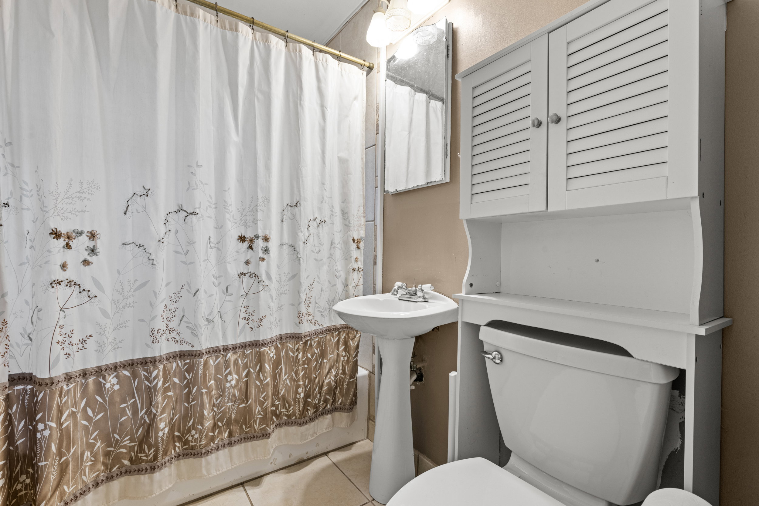 Bathroom featuring a white pedestal sink, toilet, and a white over-the-toilet storage cabinet with louvered doors