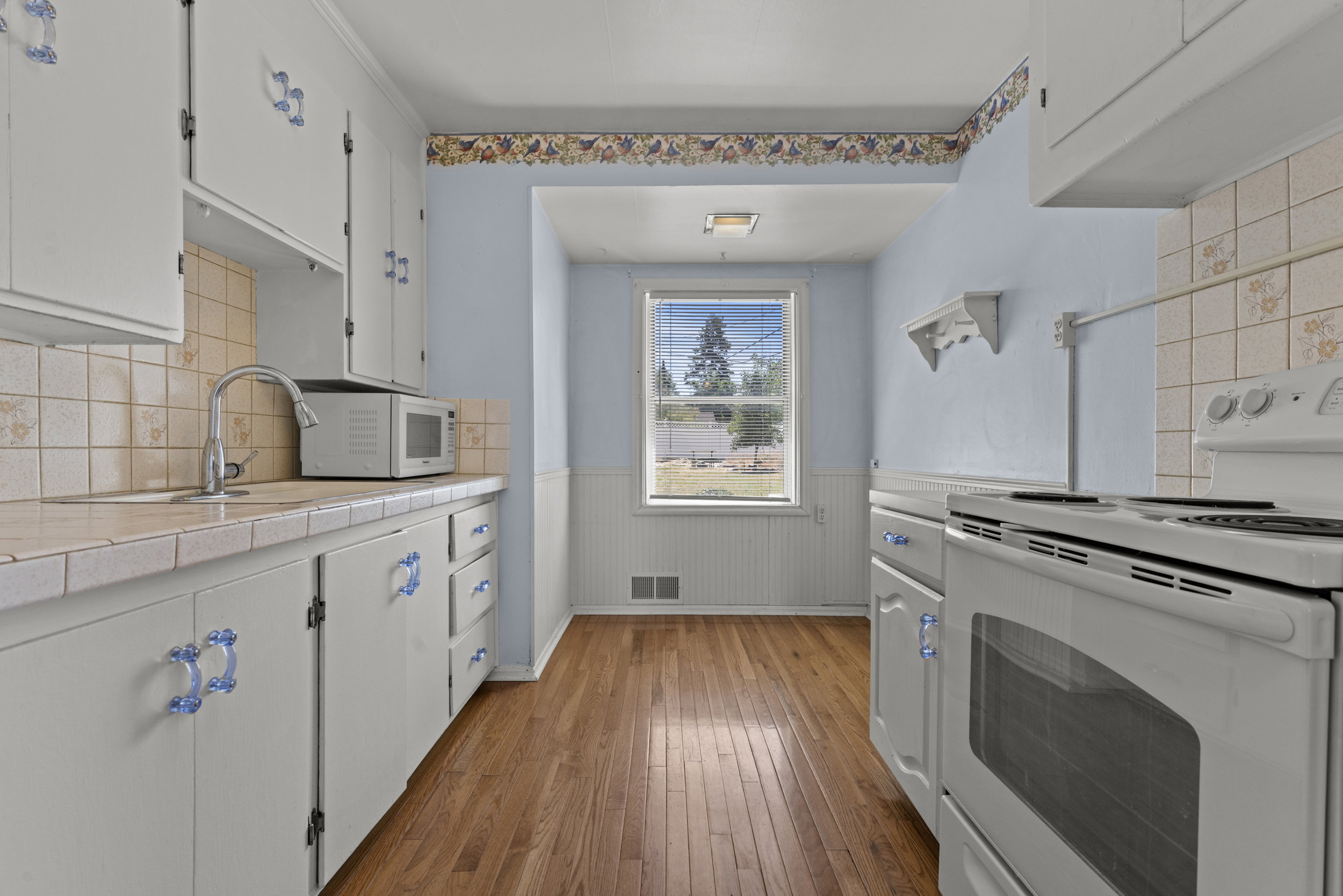 Kitchen featuring wood-finish flooring, white cabinetry with blue decorative pulls, a white electric range, and a window with exterior views