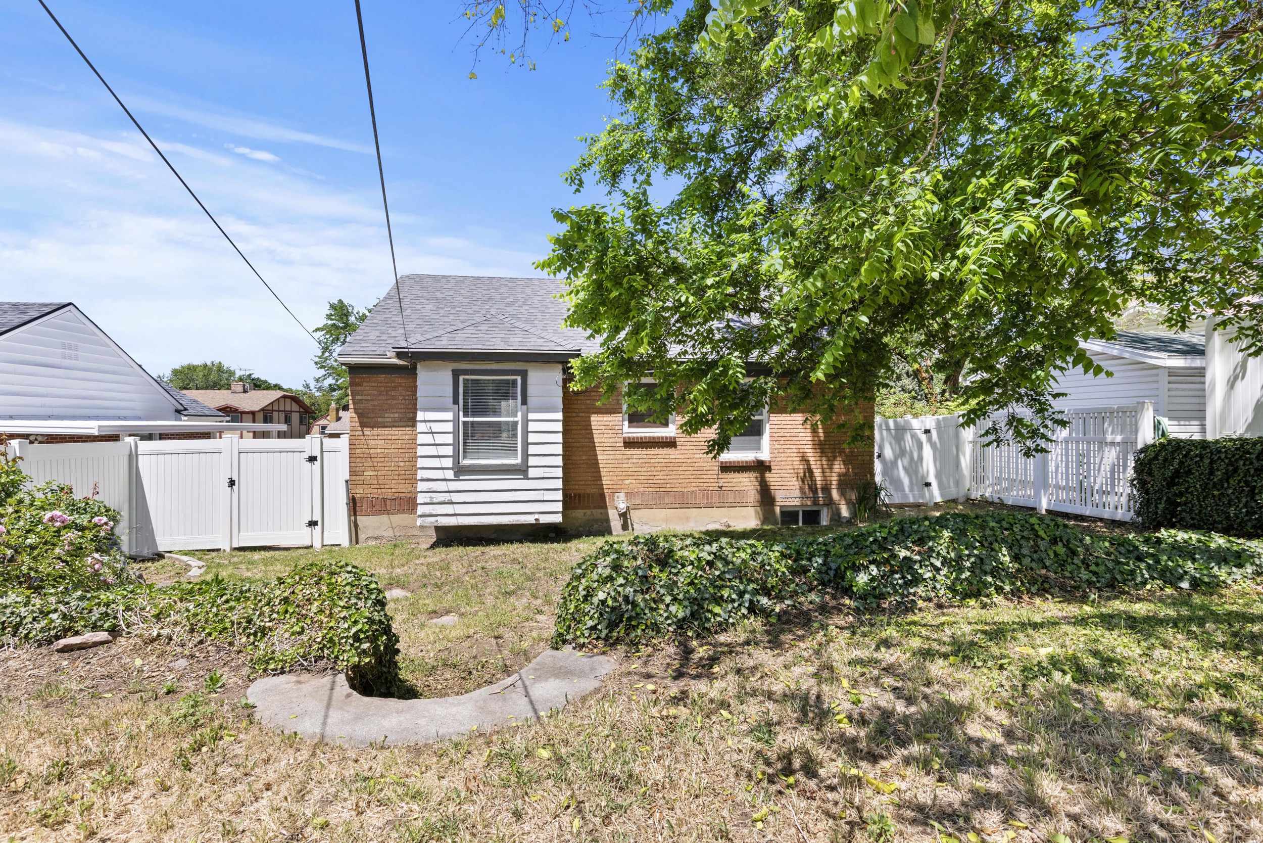 Rear exterior featuring brick and horizontal siding, a gabled roofline, and a white privacy fence